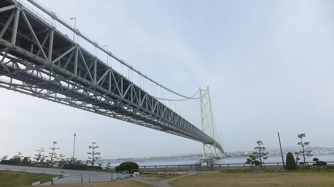 The Akashi Kaikyo Bridge sweeping across the strait, seen from the Awaji Island shore with a coastal park in the foreground
