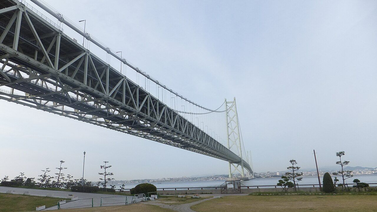 The Akashi Kaikyo Bridge sweeping across the strait, seen from the Awaji Island shore with a coastal park in the foreground