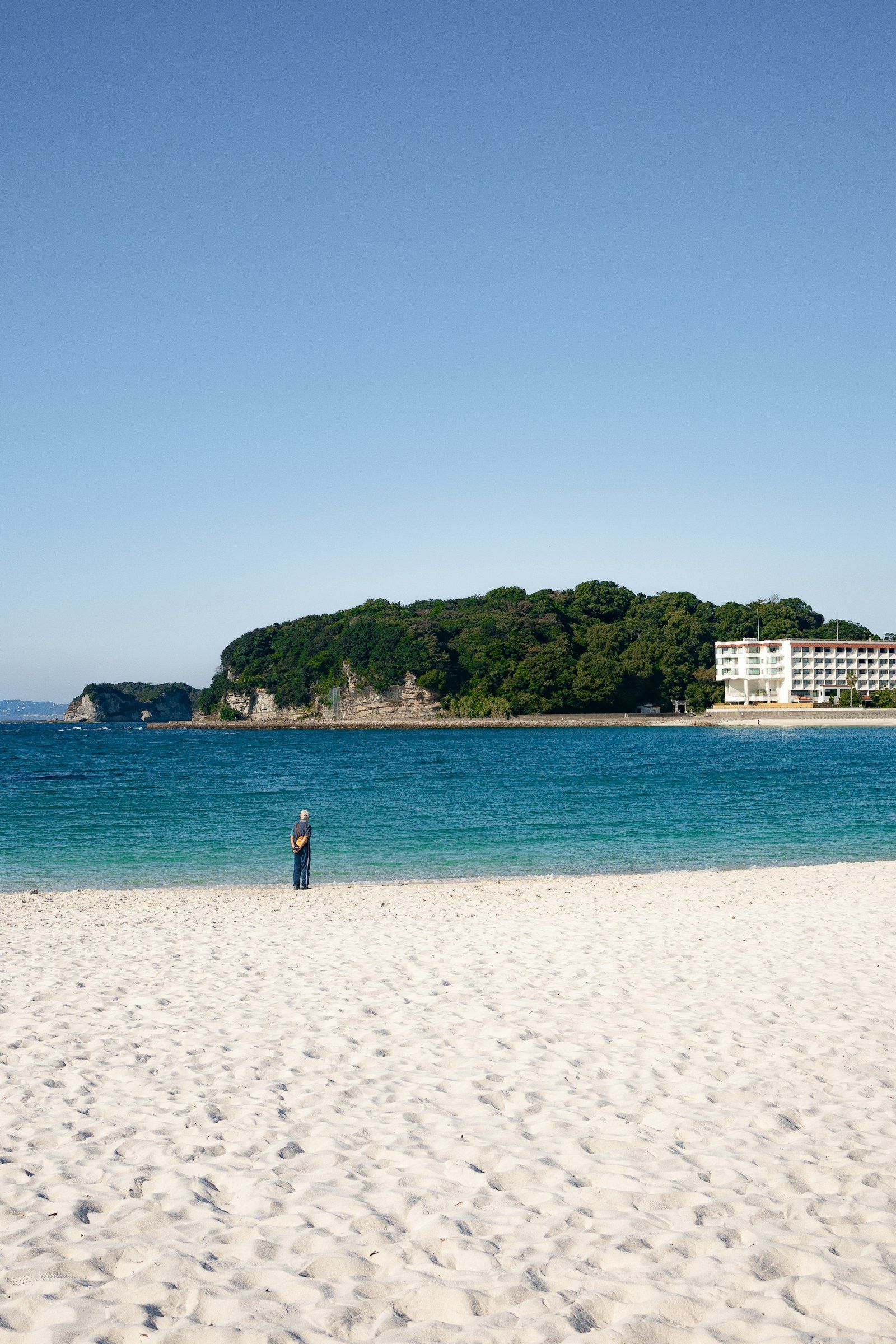 A lone visitor on the white sand of Shirarahama Beach, Shirahama, with turquoise water beyond